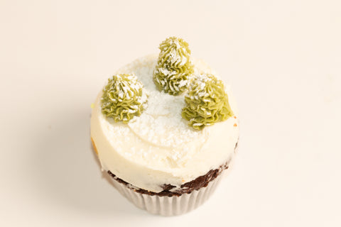 Chocolate cupcake topped with white frosting and three snow-dusted green frosting trees, creating a winter forest scene
