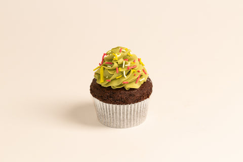 Chocolate cupcake with piped green frosting decorated as a Christmas tree, topped with festive red, yellow, and white sprinkles