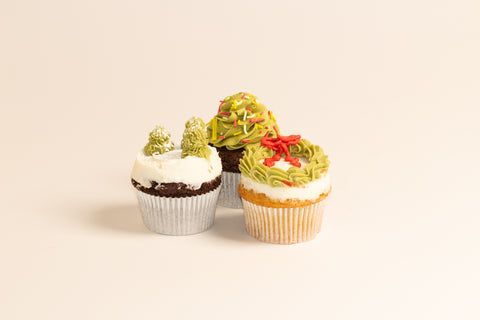 Group of three holiday cupcakes featuring different designs: snow-covered trees, sprinkled Christmas tree, and festive wreath