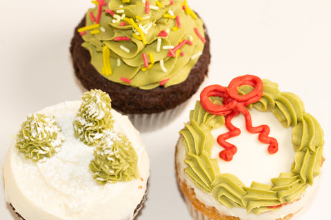 Close-up overhead view of three Christmas cupcakes showing detailed holiday designs including wreath, trees, and sprinkled decorations