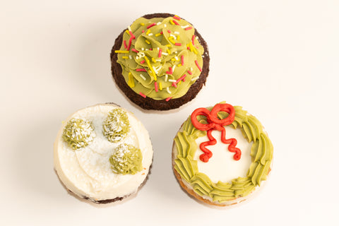 Close-up overhead view of three Christmas cupcakes showing detailed holiday designs including wreath, trees, and sprinkled decorations