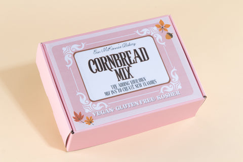 Closed pink packaging box of Erin McKenna's Bakery Cornbread Mix with decorative autumn leaves showing vegan, gluten-free, and kosher certification on beige background