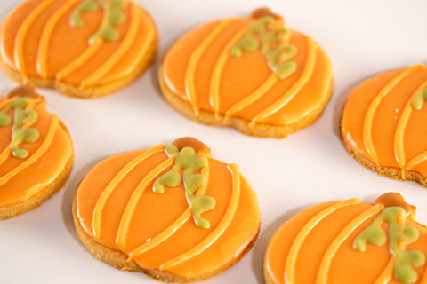 Close-up of orange pumpkin-shaped Halloween sugar cookies decorated with bright orange icing and green vines.