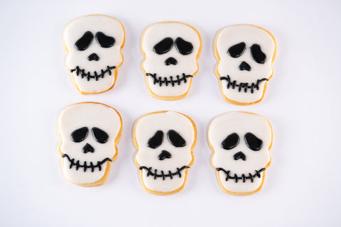 Skull-shaped sugar cookies with white icing and black details for the eyes, nose, and stitched mouth.