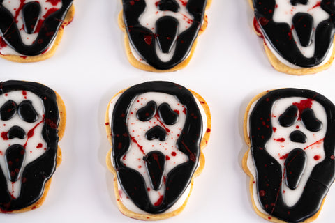 Ghost-faced sugar cookies decorated with black and white icing, featuring splashes of red for a spooky effect.