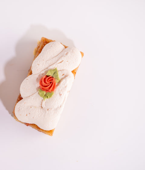 A rectangular strawberry shortcake decorated with a piped rose with green leaves on a white background.