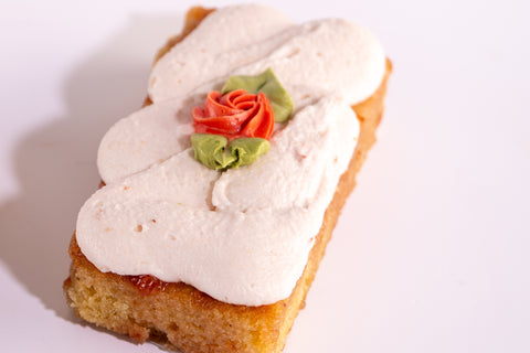 A rectangular strawberry shortcake decorated with a piped rose with green leaves on a white background.