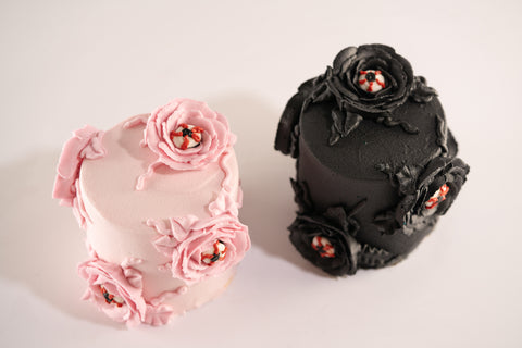 Two Halloween-themed mini cakes, one in pink and the other in black, decorated with floral icing and creepy eyeball details.