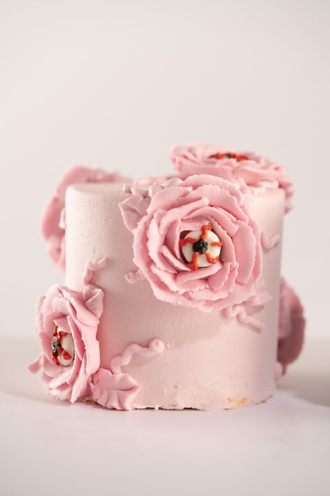 A close-up of a pink mini cake with detailed pink flowers and eerie eyeball decorations in the center.