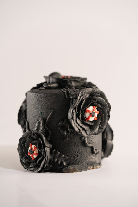 A close-up of a black mini cake with dark floral icing and eyeball decorations for a spooky effect.