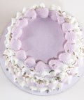 Overhead view of a round lavender cake with a ring of ridged lavender shell-piped frosting and ruffled white frosting accented with dried lavender buds, on a lavender cake board.