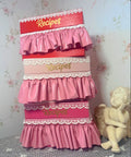 Pink recipe box with lace details on a floral wallpaper background