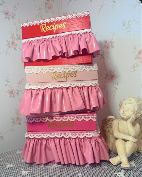 Pink recipe box with lace details on a floral wallpaper background