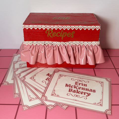 Red recipe box with lace details on a pink tile floor 