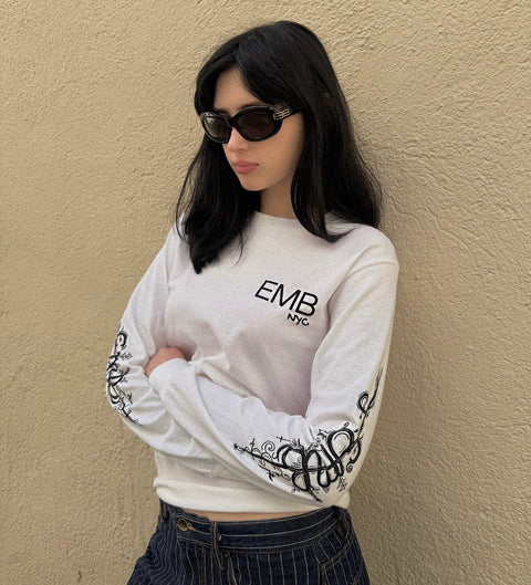 White EMB NYC long sleeve shirt with black ornamental cyber tattoo design running down both sleeves, featuring decorative flourishes and geometric patterns