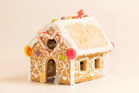 Moving animation showing decorated vegan gingerbread house featuring white icing piped in swirls and heart patterns, red candy decorations on the sides, and colorful gummy candies along the snow-covered roofline