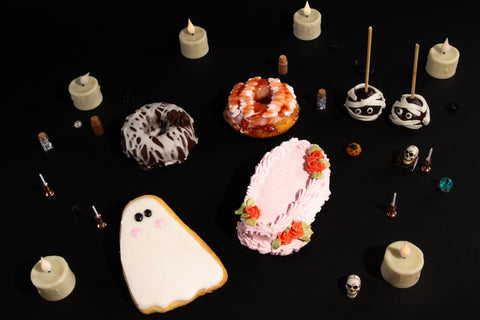 Halloween-themed treats including ghost cookies, donuts, and candles on a black background