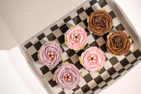 Halloween cupcakes with buttercream flowers and skulls in a box with checkered paper.