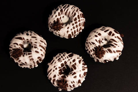 Four chocolate spider web donuts with white glaze and chocolate spider decorations arranged on black background - vegan Halloween donuts overhead 