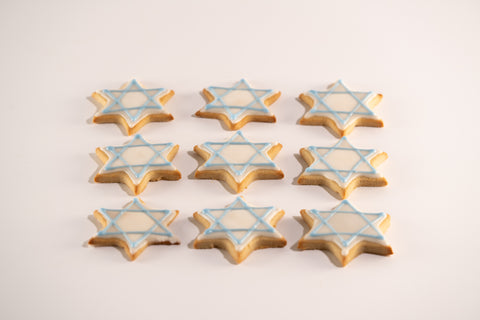 Nine Star of David sugar cookies with light blue and white icing, arranged in a 3x3 grid on a white background.