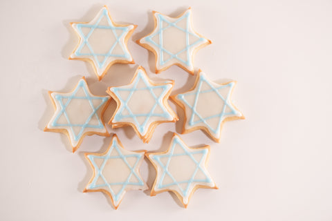 Close-up view of multiple Star of David sugar cookies with light blue and white icing, stacked and ready for serving.