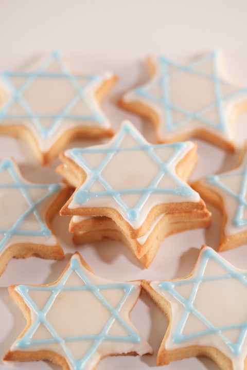 A group of six Star of David sugar cookies with light blue and white icing, stacked in a casual arrangement on a white surface.
