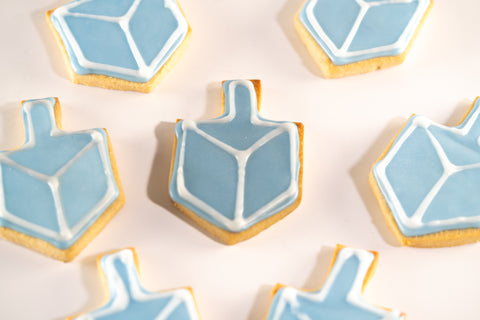 A group of dreidel-shaped sugar cookies with light blue and white icing, arranged casually on a white background