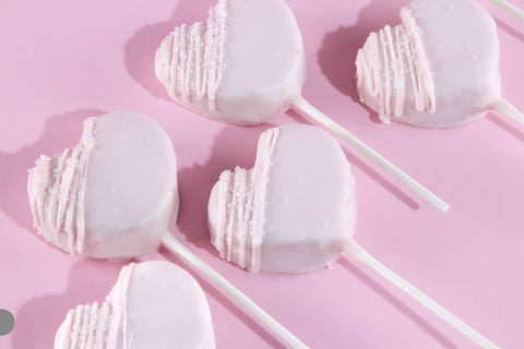 Heart-shaped vegan cake pops with white chocolate coating and pink drizzle on pink background