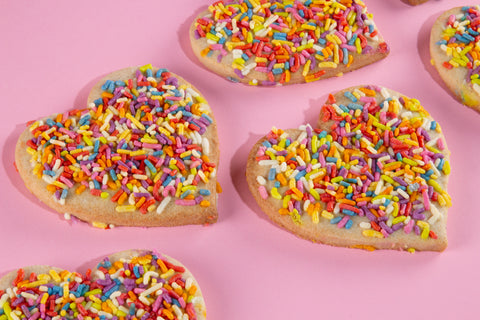 Heart-shaped cookies with colorful sprinkles on a pink background