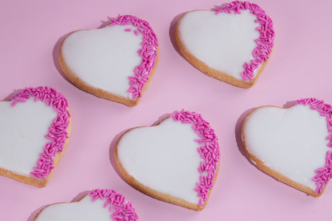 Heart-shaped sugar cookies decorated with white royal icing and pink sprinkles arranged on pink background