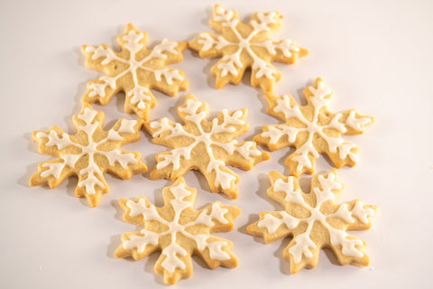 A batch of star-shaped snowflake cookies, intricately decorated with white icing, arranged in a visually appealing pattern.