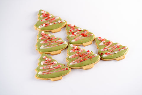  A set of Christmas tree-shaped cookies frosted with green icing and decorated with red sprinkles and white drizzles, laid out in a festive holiday display.