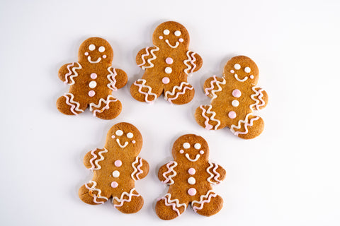 Five decorated gingerbread cookies shaped like smiling people, each adorned with pink and white icing.