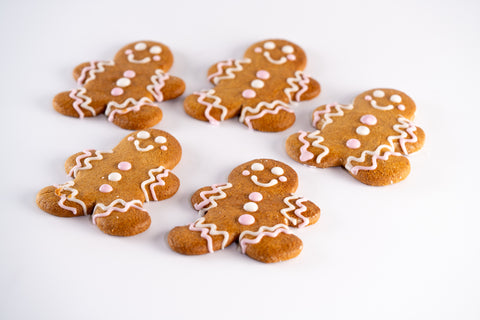 Five decorated gingerbread cookies shaped like smiling people, each adorned with pink and white icing.