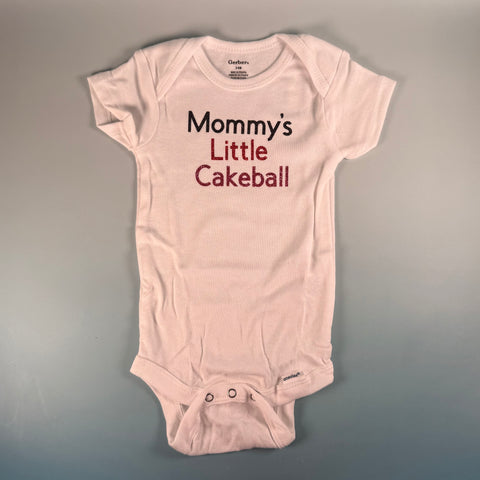 Pink baby onesie with 'Mommy's Little Cakeball' text on a gray background