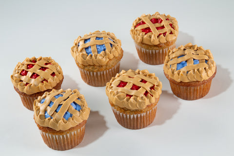 Six vegan and gluten-free Strawberry & Blueberry Pie Cupcakes with golden lattice frosting and red and blue frosting, arranged on a light gray background.