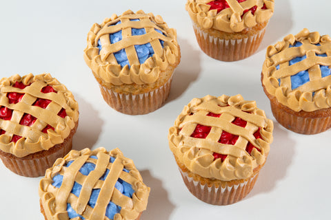 Close-up of six Strawberry & Blueberry Pie Cupcakes with golden piped lattice tops, ruffled shell borders, and red and blue frosting filling, on a light gray background.