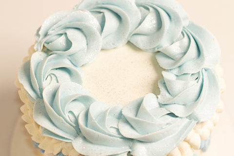 Close-up of ice blue rosette wreath with sparkling sugar crystals atop white cake with vintage-inspired frosting details