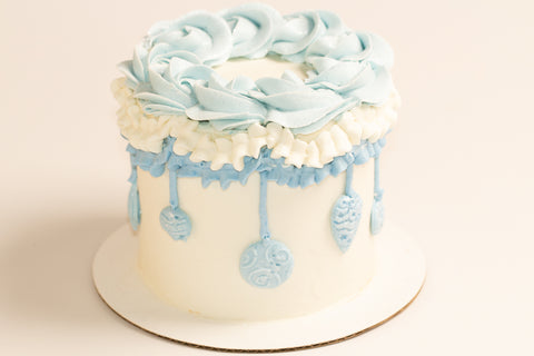 Side view of mini holiday cake featuring delicate blue ornament decorations hanging from white and powder blue ruffled bands