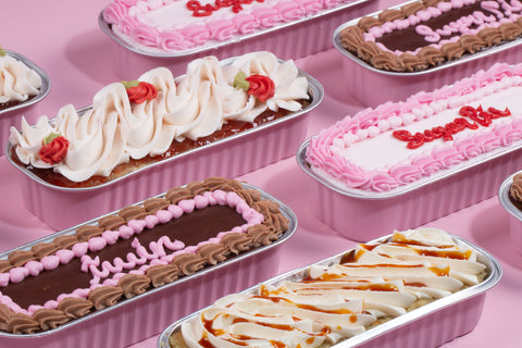 A group of mini cakescakes arranged on pink background: pink-frosted vanilla, caramel-drizzled tres leches, and chocolate raspberry with decorative piping