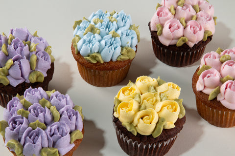 Decorative cupcakes with floral icing in various colors on a white background