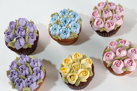 Six cupcakes with floral frosting in various colors on a white background
