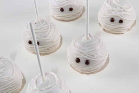 Mummy-themed cake pops decorated with white icing and small chocolate eyes, shown on a clean white background.