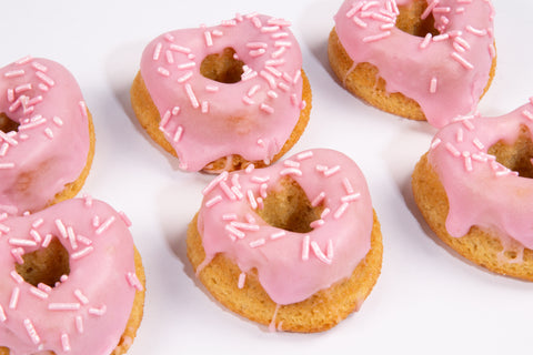 Heart-shaped mini vanilla donuts with pink glaze and white sprinkles arranged on white background