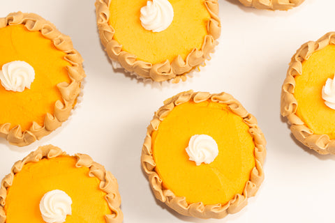 Overhead view of vegan pumpkin pie cupcakes showing detailed ruffled frosting borders around bright orange filling and decorative white cream dollops