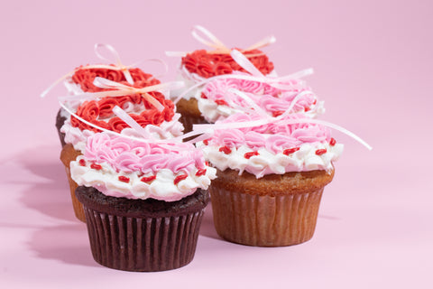 Chocolate and vanilla cupcakes decorated with pink buttercream frosting and white ribbon bows, set against a pastel pink background.