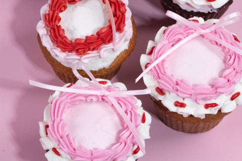 Chocolate and vanilla cupcakes decorated with pink buttercream frosting and white ribbon bows, set against a pastel pink background.