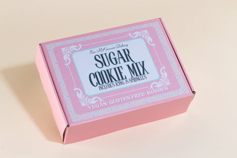 Closed pink packaging box of Erin McKenna's Bakery Sugar Cookie Mix with colorful sprinkle border design showing vegan, gluten-free, and kosher certification, includes icing and sprinkles
