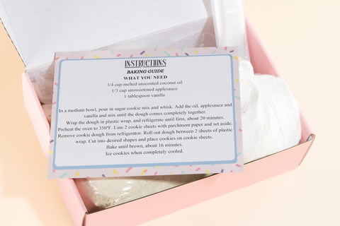 Open pink box revealing Erin McKenna's Bakery Sugar Cookie Mix contents including baking mix in clear bag, instruction card with festive sprinkle border, and decorating supplies