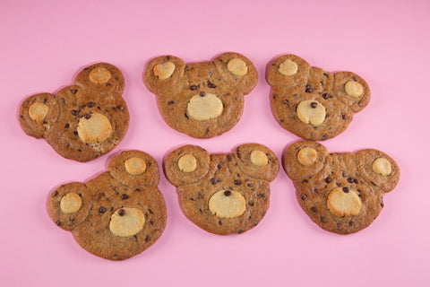 Six bear-shaped cookies with chocolate chips on a pink background